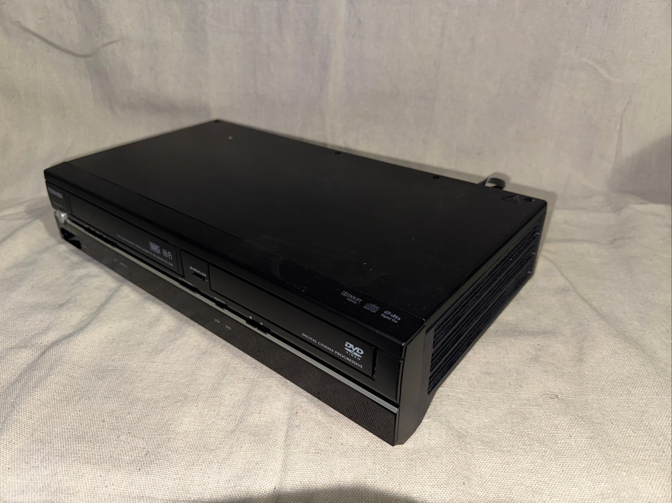 Serviced Toshiba SD-V296 DVD VHS Recorder With Remote showing top view on beige fabric background.