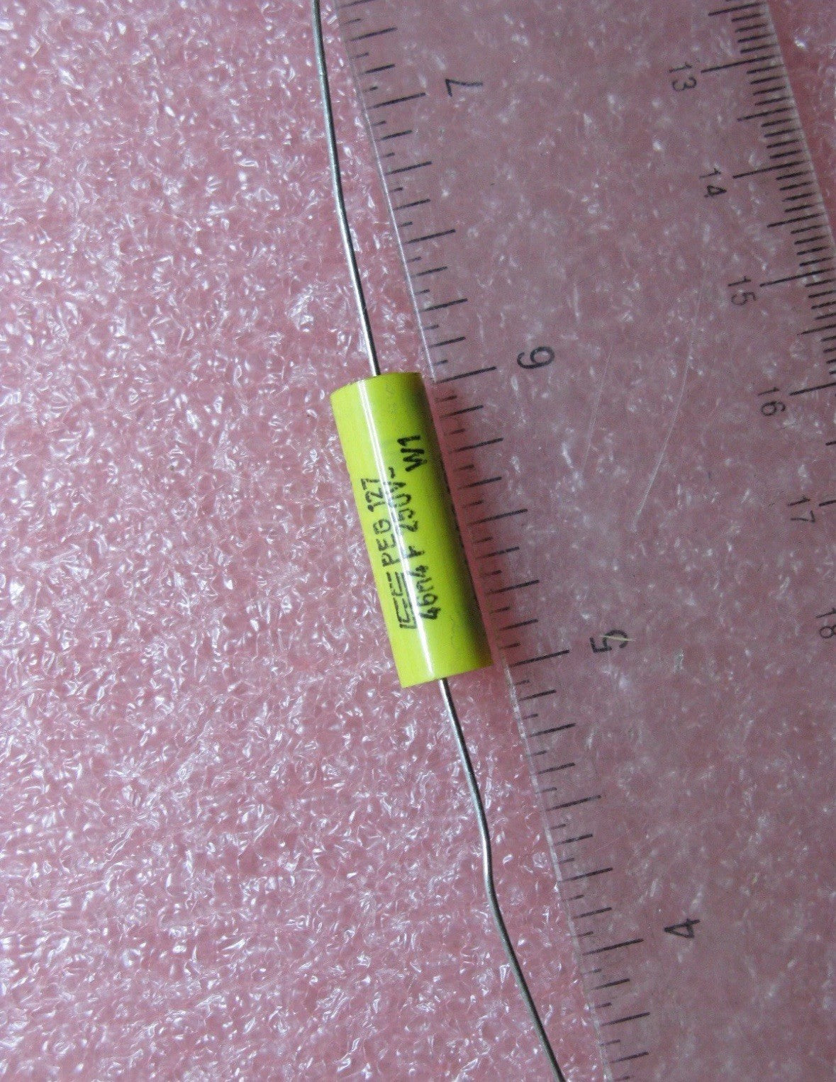 Lot of 10 PEG12746N4F250 46.4nF 250V Precision High-Stability Capacitors against a pink background with a ruler for scale.